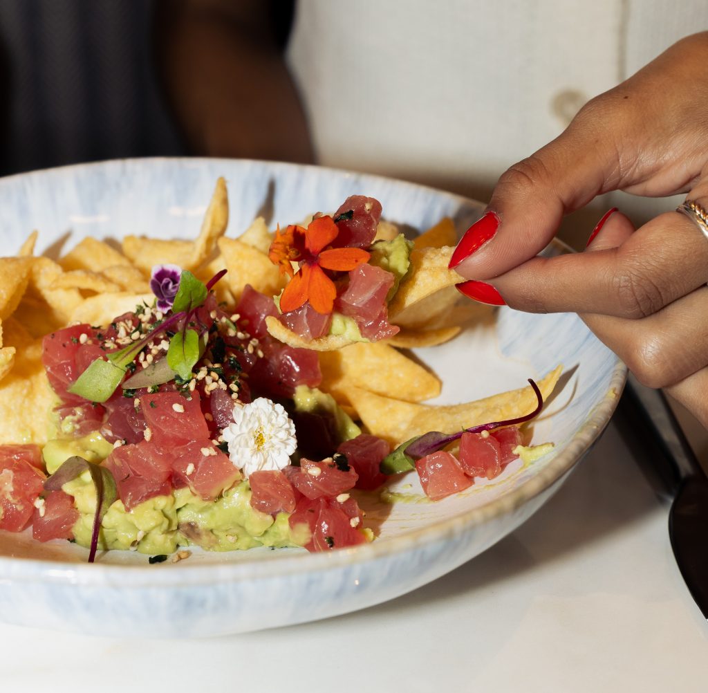 close up shot of a woman scooping tuna tartare onto a chip