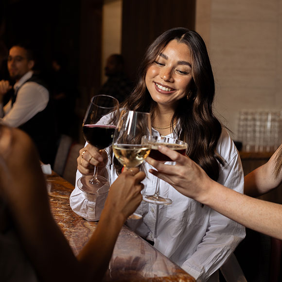 close up shot of a woman drinking wine and clinking glasses with two other women